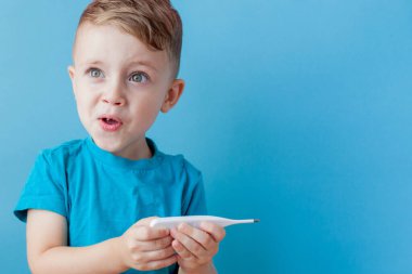 Termometresi olan hasta bir çocuk ateşinin yüksekliğini ölçüyor ve kameraya bakıyor.