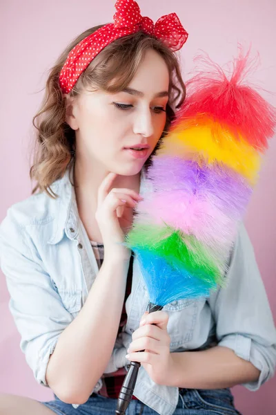 Cleaning pin up woman. Smiling pinup girl holds colorful duster brush. Cleaning service. Pin-up girl cleaner with feather duster. Retro woman with cleaning sweep. Selective focus on synthetic duster