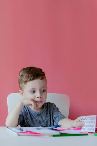 Ritratto di ragazzo carino a casa a fare i compiti. Piccolo bambino concentrato che scrive con matita colorata, in casa. Scuola elementare e istruzione. Kid imparare a scrivere lettere e numeri — Foto Stock