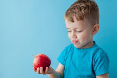 Bebek kucağında, mavi arka planda kırmızı elma yiyor.