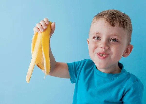 Little Boy Segurando e comendo uma banana no fundo azul, comida — Fotografia de Stock