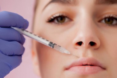 Eldivenli doktor, kadına pembe arka planda dudaklarına botoks yapıyor.