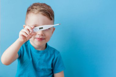 Termometresi olan hasta bir çocuk ateşinin yüksekliğini ölçüyor ve kameraya bakıyor.