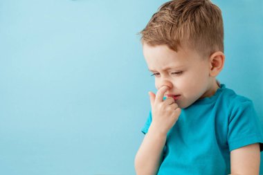 Küçük beyaz çocuk mavi arka planda burnunu karıştırıyor.