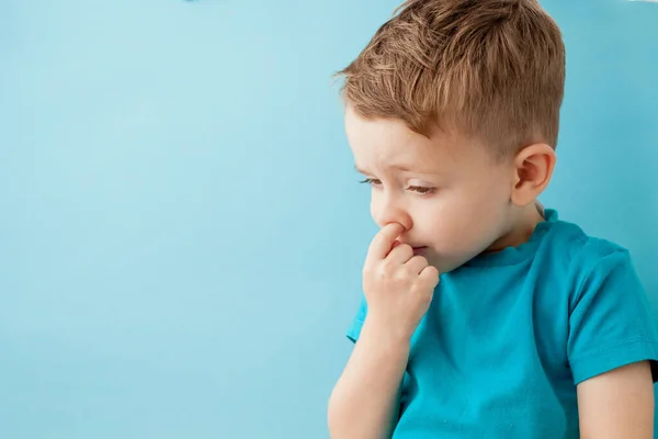 Küçük beyaz çocuk mavi arka planda burnunu karıştırıyor. — Stok fotoğraf