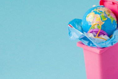 Dünya küresi çöpte yatıyor. Küre bir yığın plast içinde yatıyor.