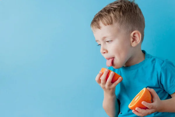 Menino segurando uma laranja em suas mãos no fundo azul, di — Fotografia de Stock