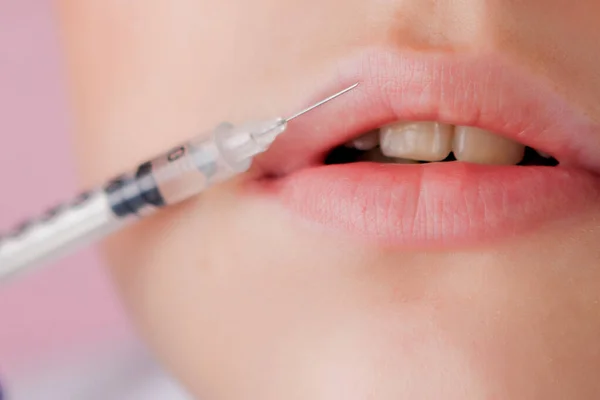 Dokter in handschoenen geven vrouw botox injecties in de lippen, op roze achtergrond — Stockfoto