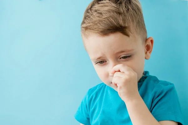 Liten kaukasisk pojke petar näsan på blå bakgrund — Stockfoto