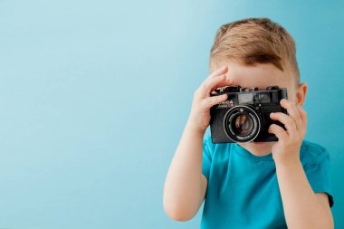 Mavi arka planda eski bir kamerası olan küçük bir çocuk.