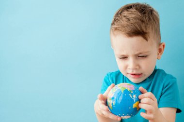 Küçük çocuk mavi arka planda bir küre tutuyor.