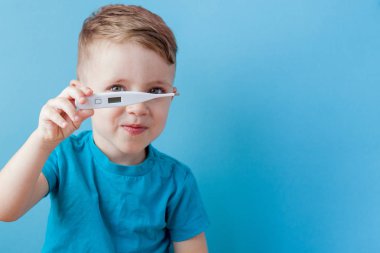 Termometresi olan hasta bir çocuk ateşinin yüksekliğini ölçüyor ve kameraya bakıyor.