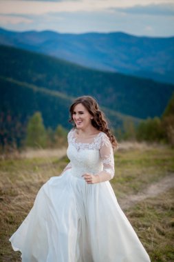 Güzel bir düğün çifti, gelin ve damat, dağların arka planında aşıklar. Güzel takım elbiseli damat ve beyaz lüks elbiseli gelin. Düğün çifti yürüyor.