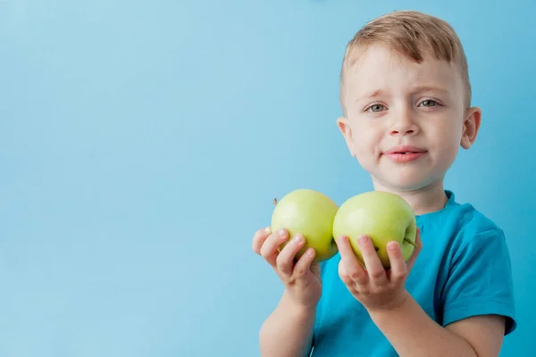 Маленький хлопчик тримає яблука в руках на синьому фоні, дієту і вправи для здорового способу життя — стокове фото