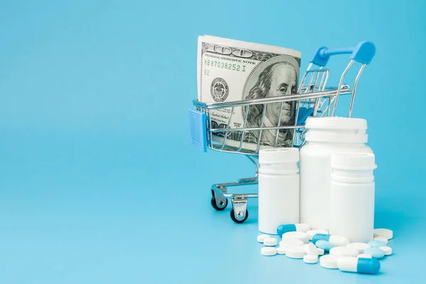 Scattered pharmaceutical medicine pills, tablets and capsules on dollar money isolated on blue background. Medicine expenses. — Stock Photo, Image
