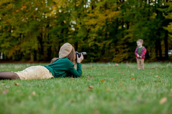 Mulher fotógrafa fotografa a criança para passar fora no parque — Fotografia de Stock