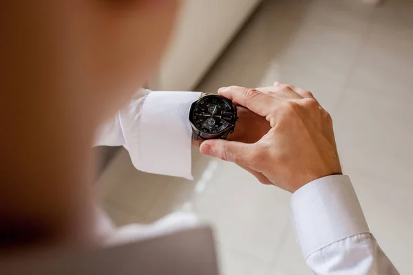 El novio mira su reloj para comprobar la hora. El reloj está puesto en la mano del hombre. Preparación matutina del novio antes de la boda — Foto de Stock