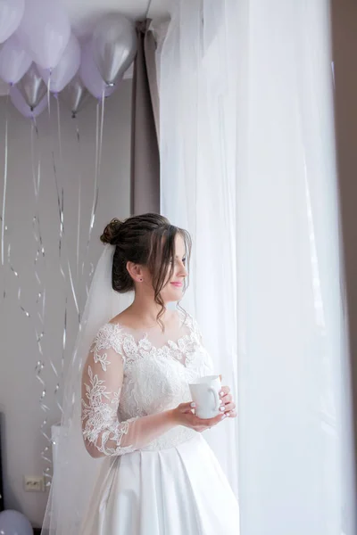 Молодая красивая девушка невеста в пеньюар у подоконника с чашкой кофе и ждет жениха, утро невесты, день свадьбы . — стоковое фото