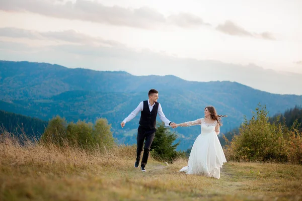 Felice splendida sposa ed elegante sposo correre e divertirsi, coppia di nozze, cerimonia di lusso in montagna con vista mozzafiato — Foto Stock