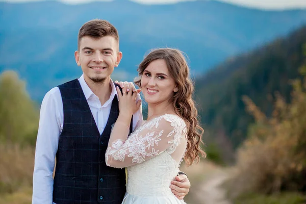 Beautiful wedding couple, bride and groom, in love on the background of mountains. The groom in a beautiful suit and the bride in a white luxury dress. Wedding couple is walking — Stock Photo, Image