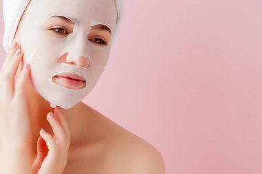 Güzel genç kadın kozmetik doku maske pembe bir arka plan üzerinde bir yüzünde uyguluyor. Sağlık ve güzellik tedavi ve teknoloji kavramı
