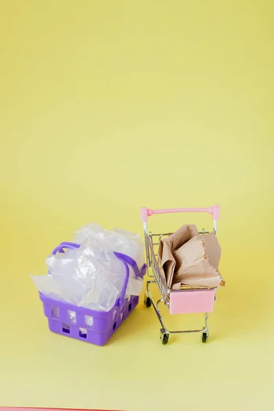 Polytheen en papieren zakken in een winkelmandje op een gele backgr — Stockfoto