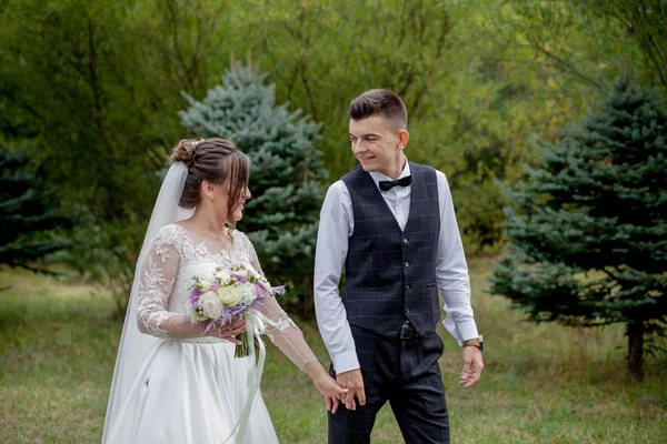 Šťastná nevěsta a ženich drží za ruce a procházky v zahradní svatební den. Zadní pohled na okouzlující stylové novomanželé držící se za ruce při procházce v parku lesa, šťastné svatební okamžiky — Stock fotografie