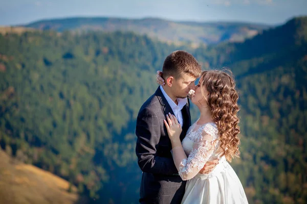 Krásné novomanželé objímající se na pozadí skal a hor. Na útesu stojí stylová nevěsta a krásná nevěsta. Svatební portrét. Rodinná fotka — Stock fotografie