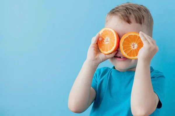 Menino segurando uma laranja em suas mãos no fundo azul, di — Fotografia de Stock