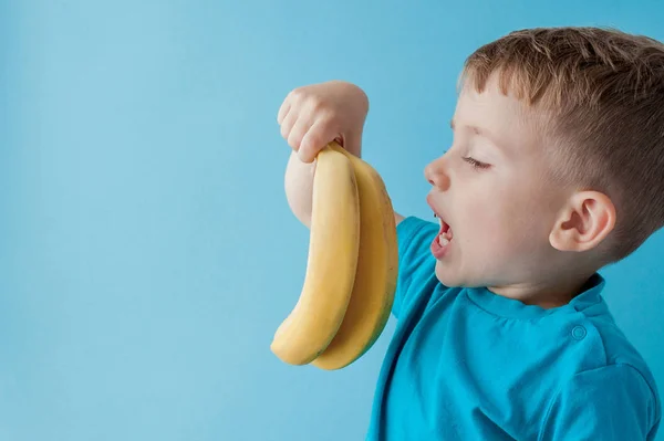 Little Boy Segurando e comendo uma banana no fundo azul, comida — Fotografia de Stock