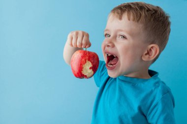 Bebek kucağında, mavi arka planda kırmızı elma yiyor.