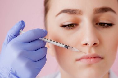 Eldivenli doktor, kadına pembe arka planda dudaklarına botoks yapıyor.