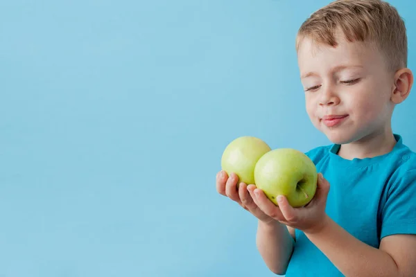Niño pequeño sosteniendo una manzana en sus manos sobre fondo azul, di — Foto de Stock