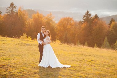 Güzel bir düğün çifti, gelin ve damat, dağların arka planında aşıklar. Güzel takım elbiseli damat ve beyaz lüks elbiseli gelin. Düğün çifti yürüyor.