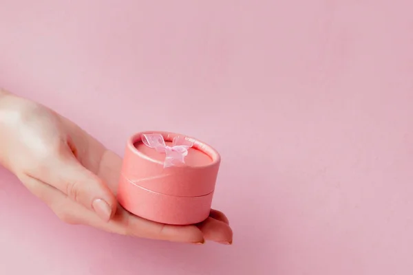 Runda rosa presentförpackning i kvinnors händer på en rosa bakgrund. Festlig koncept för alla hjärtans dag, mors dag eller födelsedag — Stockfoto