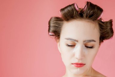Yüzüne dokunmadan bir maske ve curlers ile güzel genç kız.