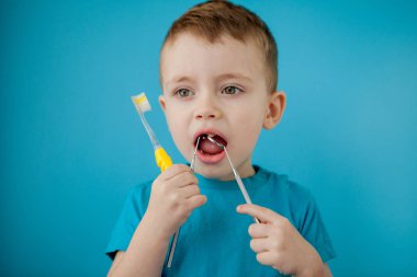 Küçük şirin çocuk mavi arka planda dişlerini fırçalıyor.