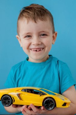 Küçük çocuk mavi arka planda büyük sarı bir arabayla oynuyor.