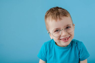 Komik gözlüklü, gülümseyen bir çocuğun portresi. - Okul. Anaokulu. Moda. Mavi arkaplanda stüdyo portresi, boşluğu kopyala
