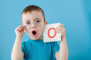 Mavi arka planı olan şirin bir çocuk. Çocuk harfleri öğreniyor. Alfabe