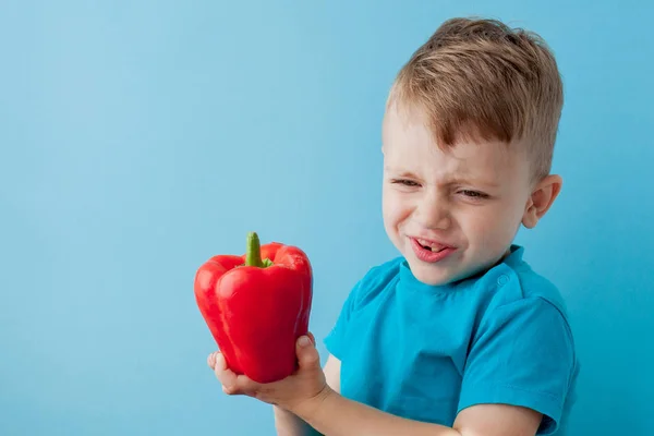 Little kid holding pepper in his hands on blue background. Vegan — Stock Photo, Image