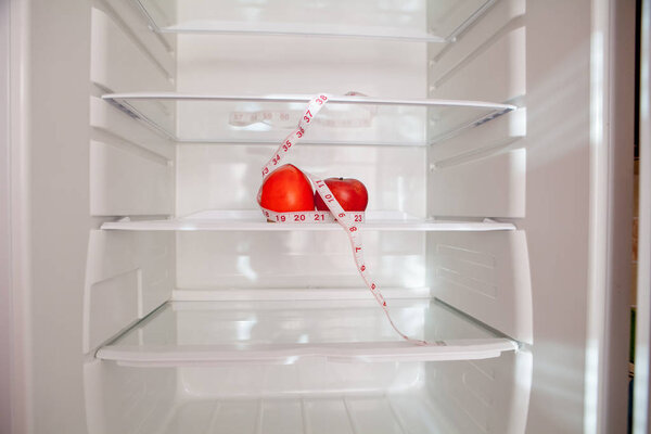 Empty refrigerator with a persimmon and green apple and tape measuring on the shelf, diet concept, blurred background