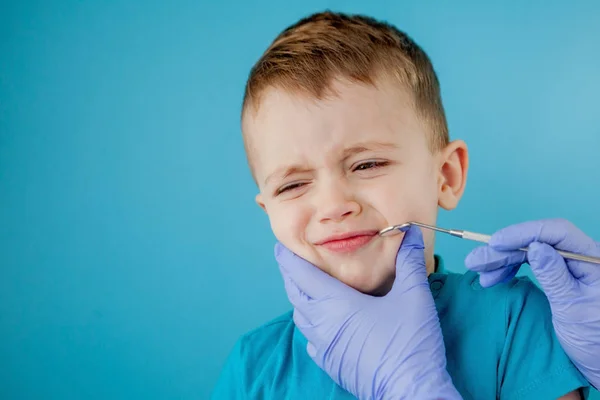 Küçük hasta mavi arka planda dişçinin ağzını açmak istemiyor. Dansçı dişleri tedavi eder. Dişçinin dişçi muayenehanesindeki küçük çocuğun dişlerini tedavi ettiği yakın plan.. — Stok fotoğraf