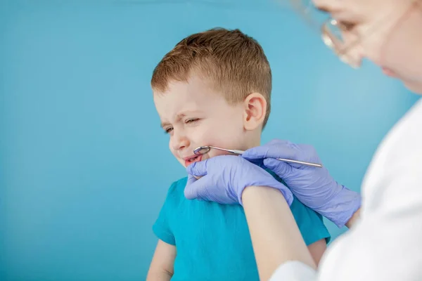 Kleine patiënt wil de mond van de tandarts niet openen op een blauwe achtergrond. Dantist behandelt tanden. close-up uitzicht op tandarts behandeling tanden van kleine jongen in tandarts kantoor. — Stockfoto