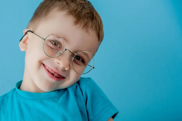Retrato de um garotinho sorridente em óculos engraçados. Na escola. Pré-escolar. Moda. Retrato de estúdio em um fundo azul, espaço de cópia — Fotografia de Stock