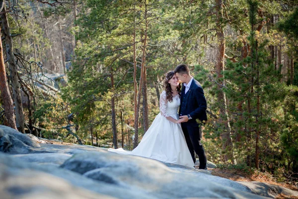 Gyönyörű friss házasok ölelkeznek a sziklák és hegyek hátterében. Stílusos menyasszony és gyönyörű menyasszony áll a sziklán. Esküvői portré. Családi fotó — Stock Fotó