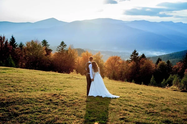 Casal de casamento bonito, noiva e noivo, no amor no fundo das montanhas. O noivo em um belo terno e a noiva em um vestido de luxo branco. Casamento casal está andando — Fotografia de Stock