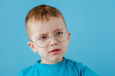 Komik gözlüklü, gülümseyen bir çocuğun portresi. - Okul. Anaokulu. Moda. Mavi arkaplanda stüdyo portresi, boşluğu kopyala