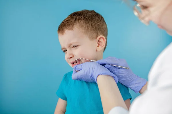 Kleine patiënt wil de mond van de tandarts niet openen op een blauwe achtergrond. Dantist behandelt tanden. close-up uitzicht op tandarts behandeling tanden van kleine jongen in tandarts kantoor. — Stockfoto