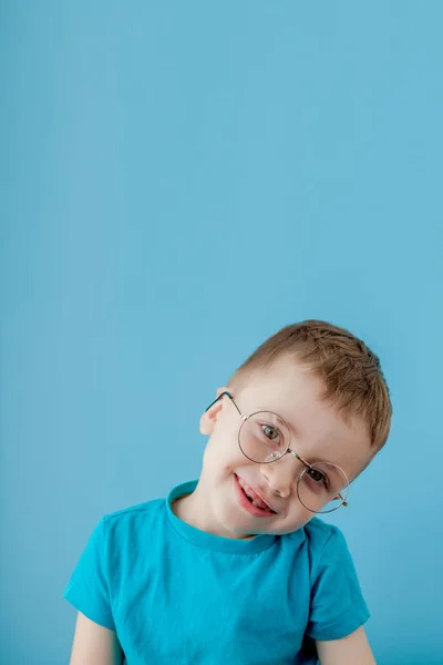 Retrato de um garotinho sorridente em óculos engraçados. Na escola. Pré-escolar. Moda. Retrato de estúdio em um fundo azul, espaço de cópia — Fotografia de Stock